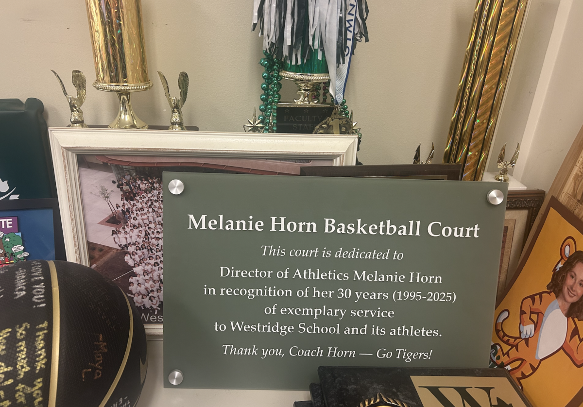 The plaque inside Coach Horn's office that announces the naming of the "Melanie Horn Basketball Court." Besides it sit trophies, other plaques, and sports merch Coach Horn has collected over the years. 